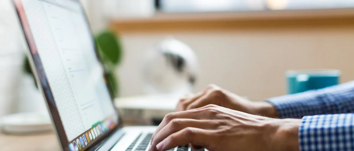 Close-up of hands typing on a laptop keyboard next to a coffee cup