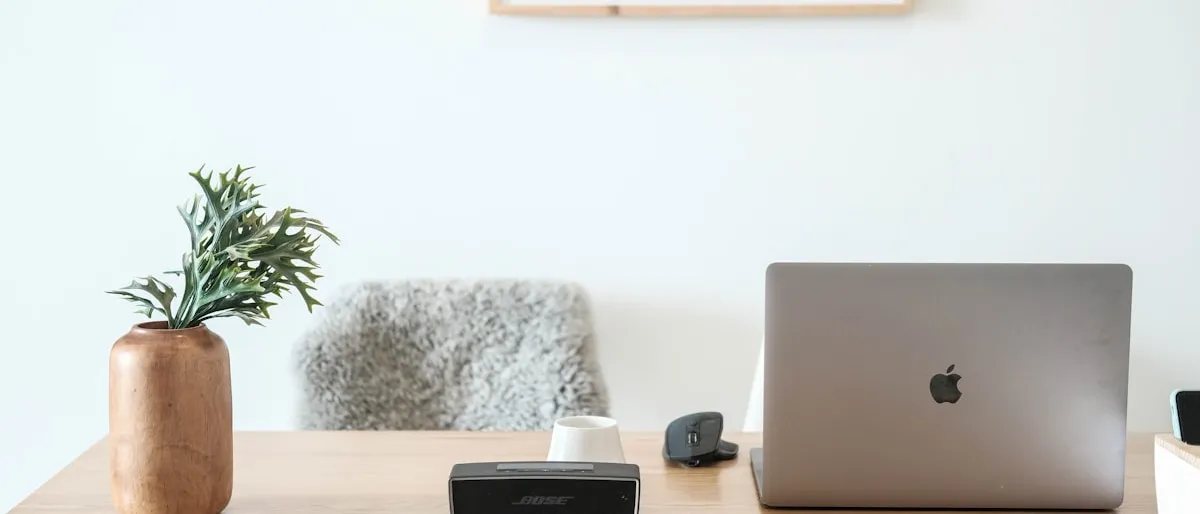 A tidy home office desk with a laptop, speaker, and small plant