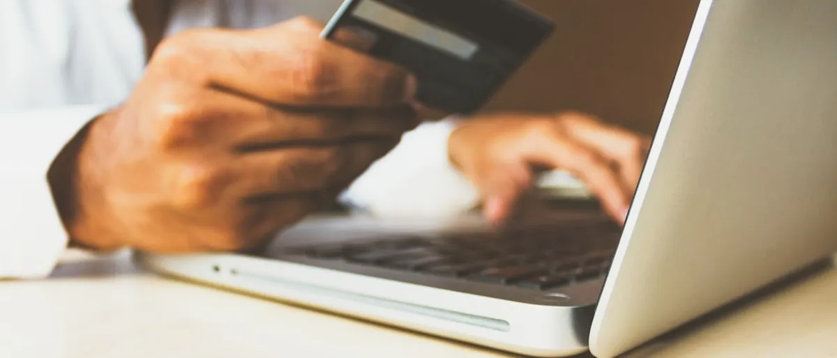 A man holding a credit card while typing on a laptop keyboard