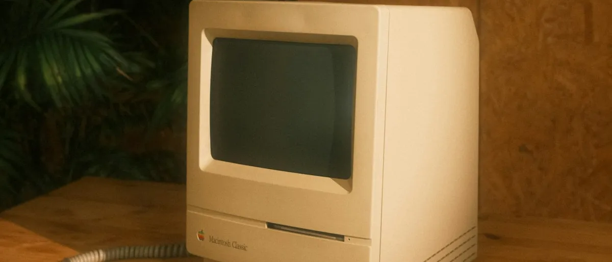 A vintage Macintosh Classic computer with its keyboard and mouse on a wooden desk