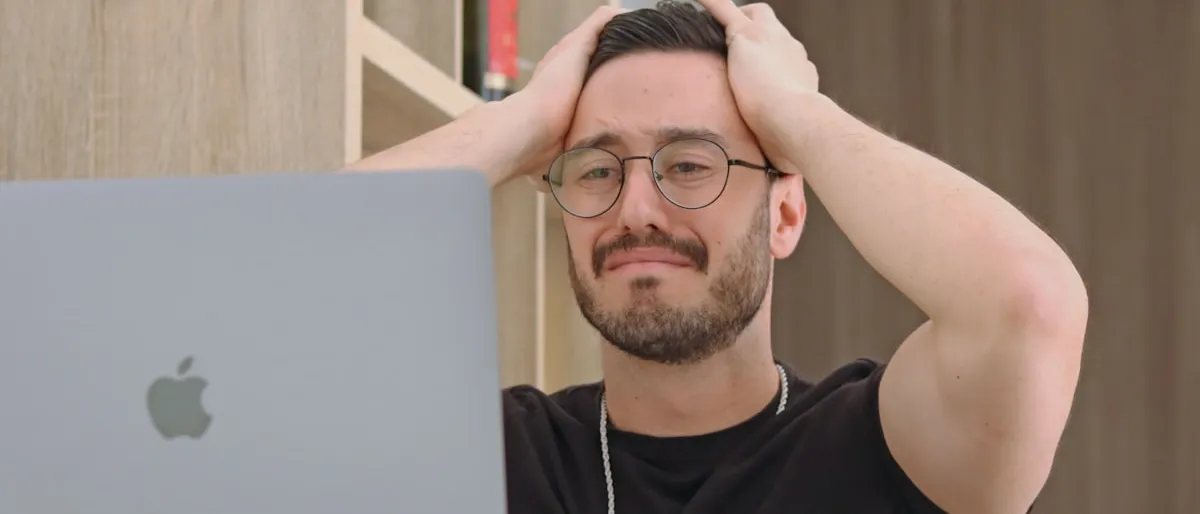 A frustrated man holding his head while looking at a laptop screen