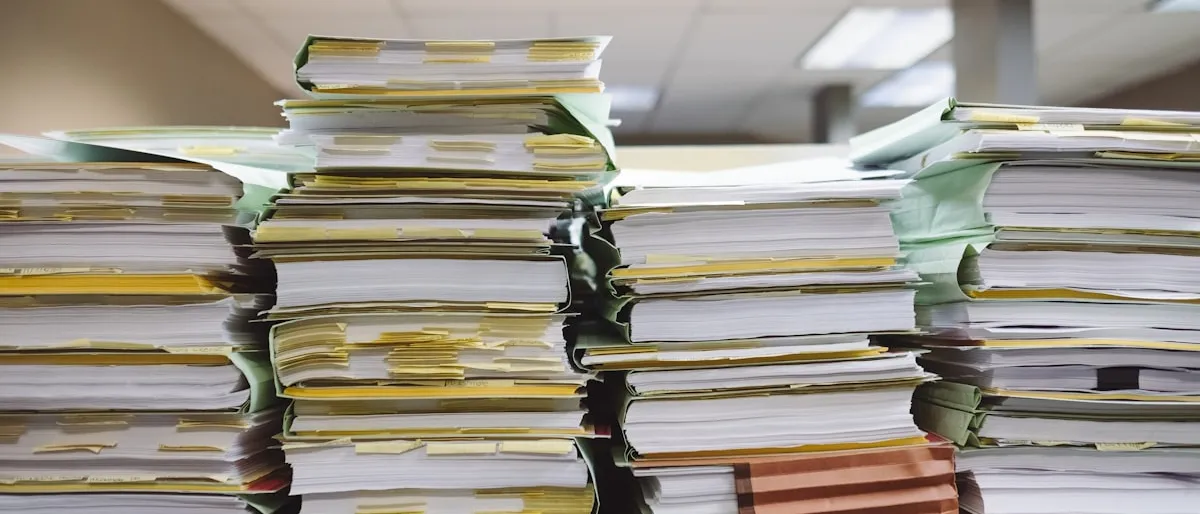 Tall stacks of disorganized paper documents and file folders in an office
